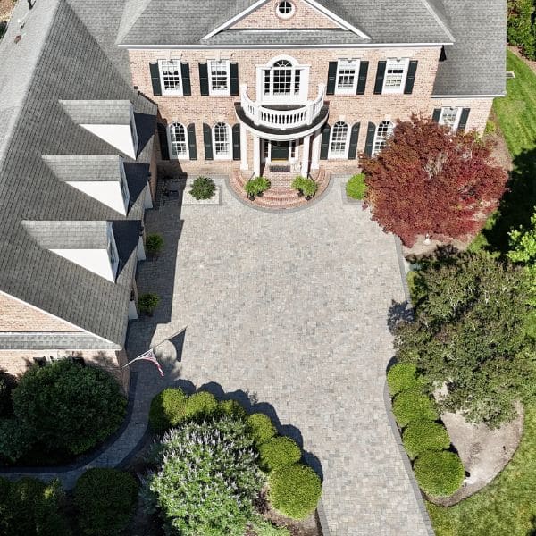 Aerial view of a large brick mansion with a curved porch, brick front steps, and a circular driveway bordered by manicured landscaping.